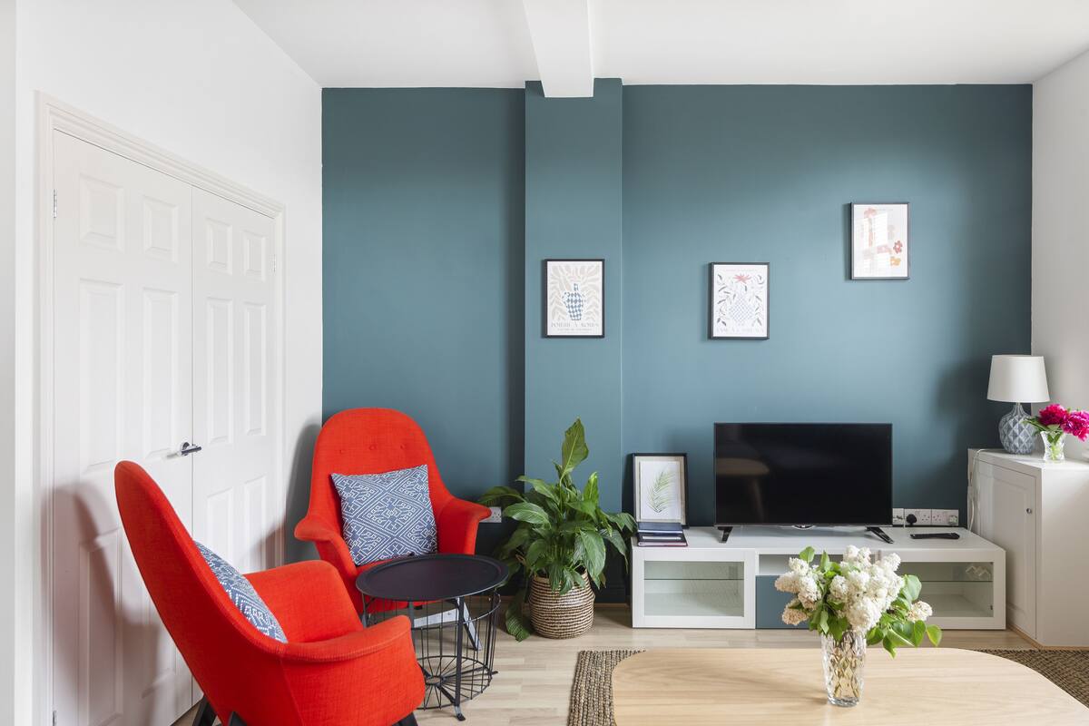 A living room with a teal wall, a red chair, a TV, and a white cabinet.