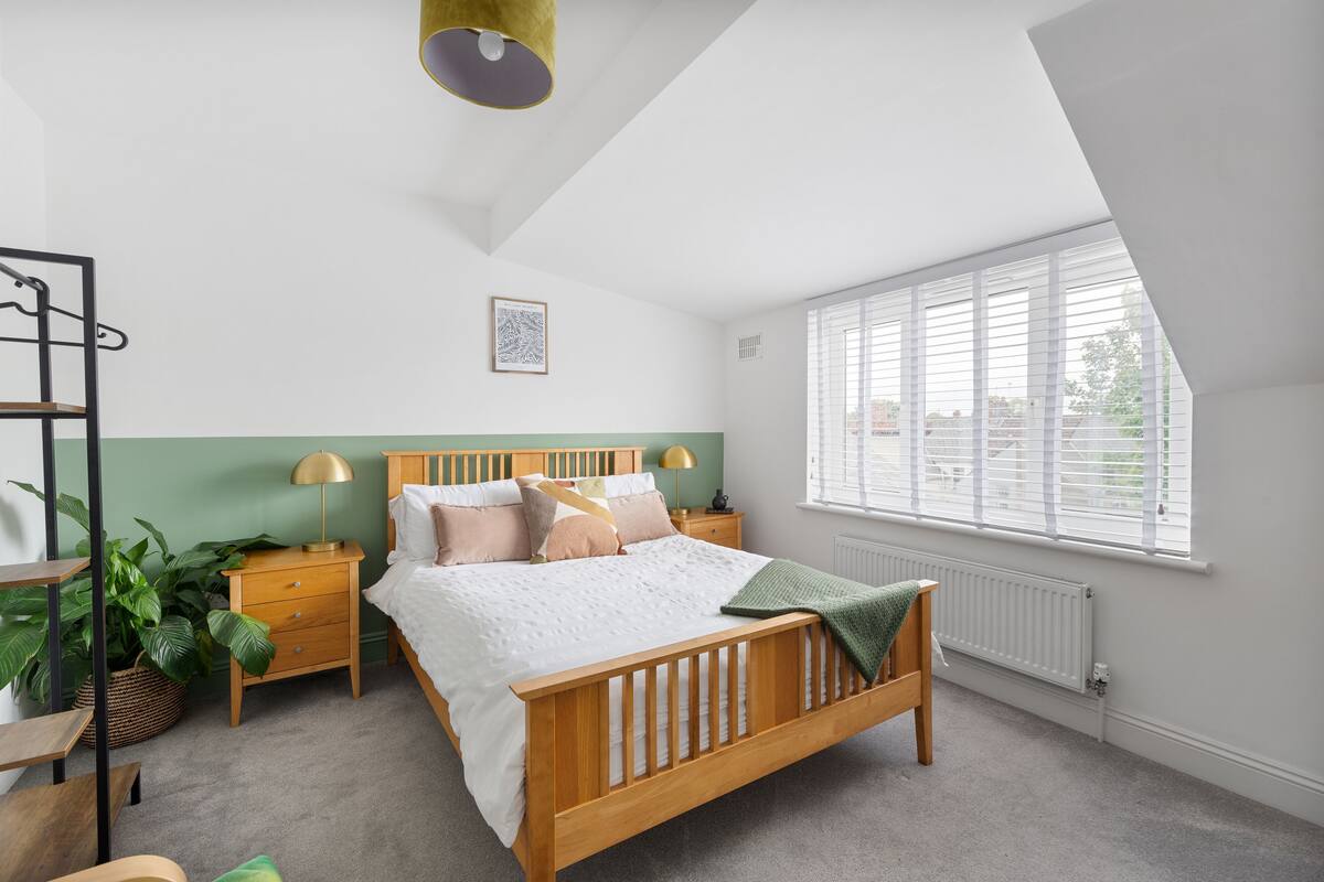 A bedroom with a wooden bed, bedside tables, a nightstand, a green plant, and a window with blinds.