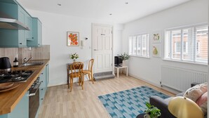 A modern kitchen with teal cabinets, a dining area with a blue patterned rug, and a living room with a sofa and a plant. - 84A Albany Road (Cardiff)