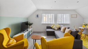 A modern living room with a grey sofa, yellow armchairs, a flat-screen TV, and a small table. - 84A Albany Road (Cardiff)