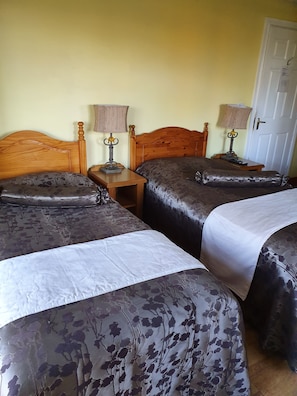 A room with two wooden beds, each with a nightstand and a lamp. The walls are painted yellow, and there is a door visible. - Golden Dawn Guesthouse (Saggart)