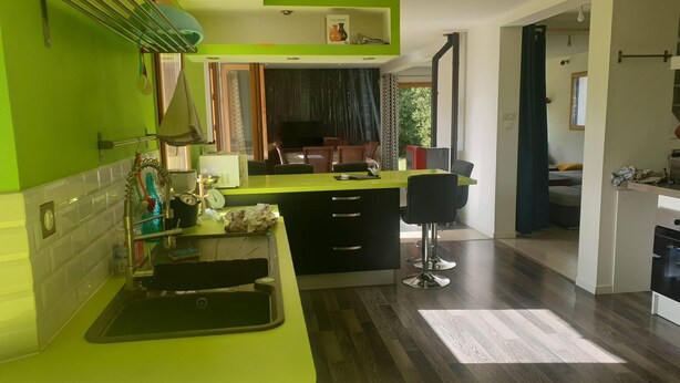 Une cuisine moderne avec un plan de travail vert, un évier et un coin repas équipé d’une chaise.