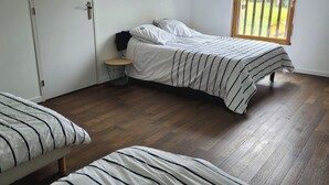 Une chambre avec deux lits, un plancher en bois, une petite table ronde et une fenêtre donnant sur un paysage verdoyant.