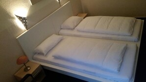 A double bed with white linens, a bedside table with a lamp, and a wall-mounted light fixture. - Hotel Garni Frankfurt (Frankfurt)