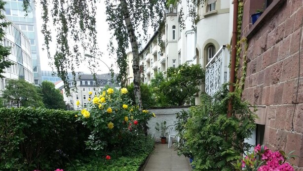 A narrow stone pathway flanked by potted plants and a white chair. - Hotel Garni Frankfurt (Frankfurt)