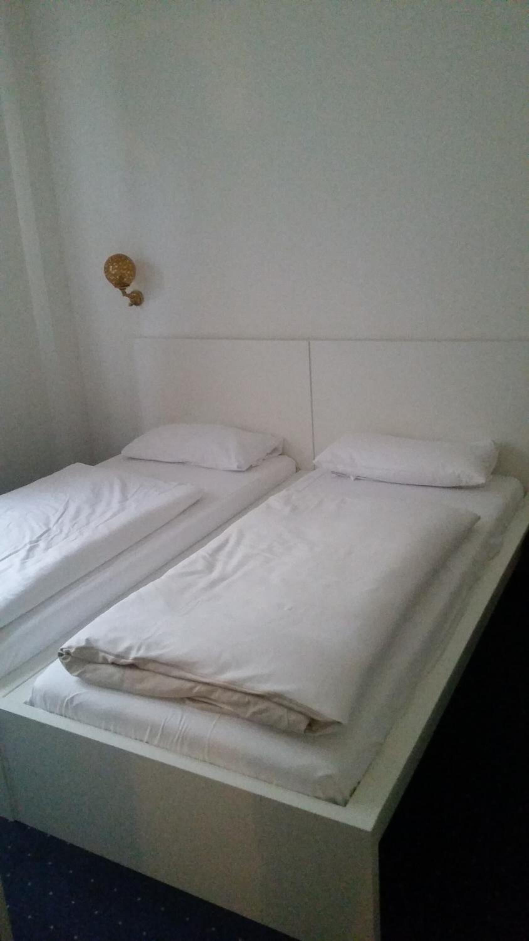 A double bed with white bedding in a room with white walls and a simple headboard.