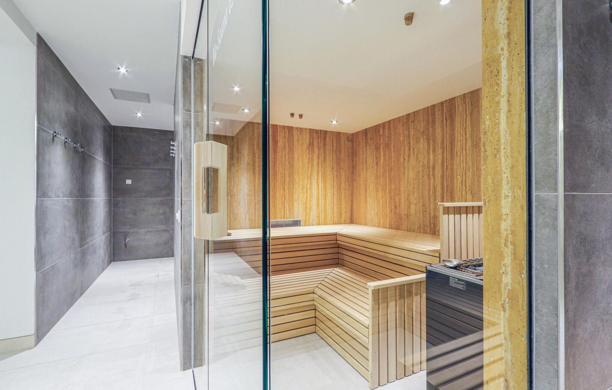 Ein modernes Badezimmer mit einer Holzbank, einer Glasabtrennung und einem sichtbaren Saunaofen.