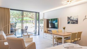 Quarto de hotel moderno com cama, escrivaninha, televisão e varanda com mobiliário de exterior.