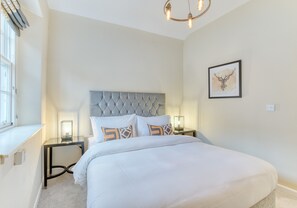 Ein Schlafzimmer mit einem großen Bett, einem gepolsterten Kopfteil, Nachttischlampen und einer Wanddekoration mit einem Hirschgeweih.