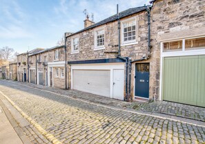 A row of stone buildings with garage doors, cobblestone street, and a clear sky. - Beautiful two-bedroom mews house situated in a city centre location in the New Town. Sleeps 5. (Edinburgh)
