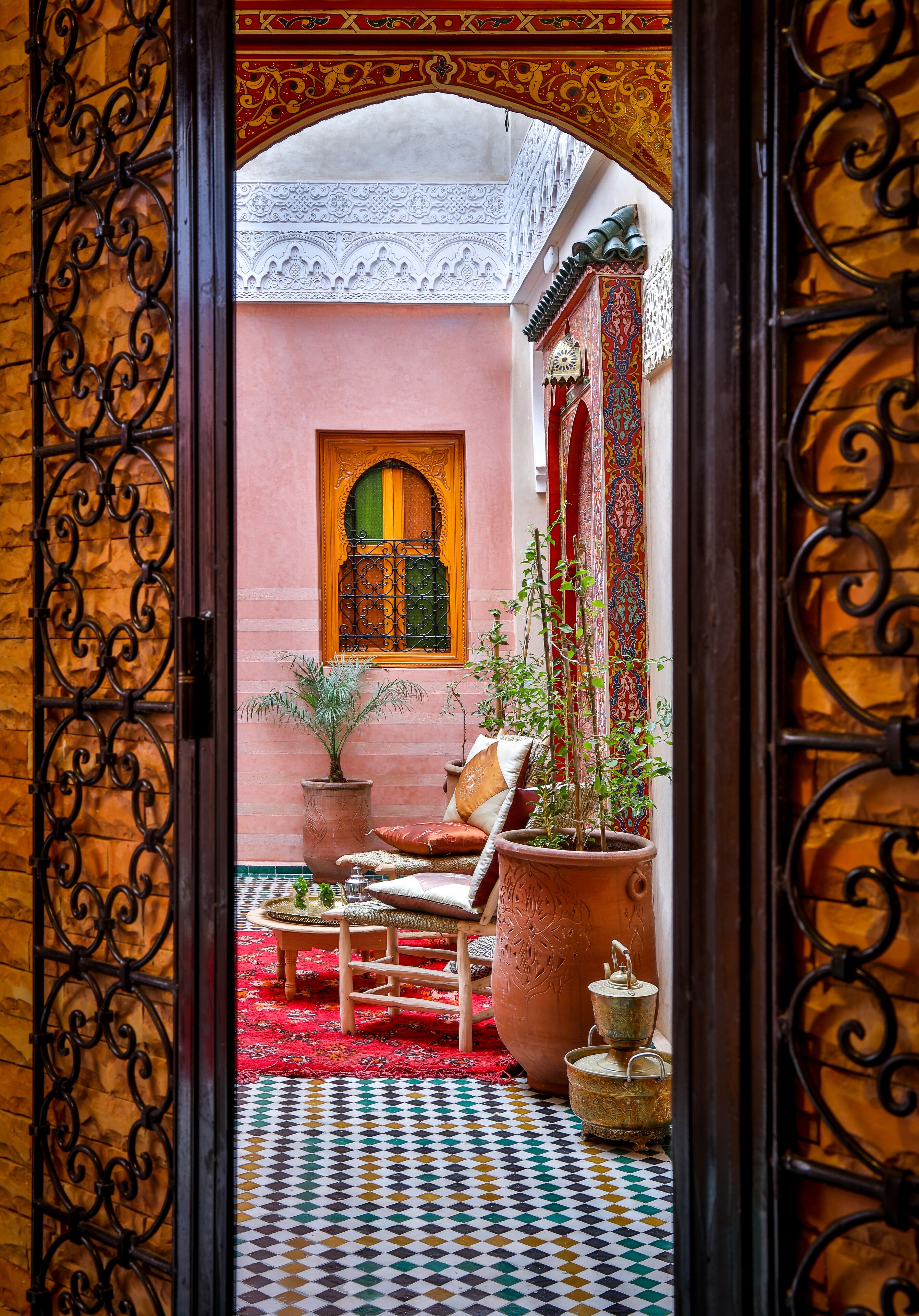Un patio interior con suelo de baldosas, un banco de madera, una planta en maceta y un muro decorativo.