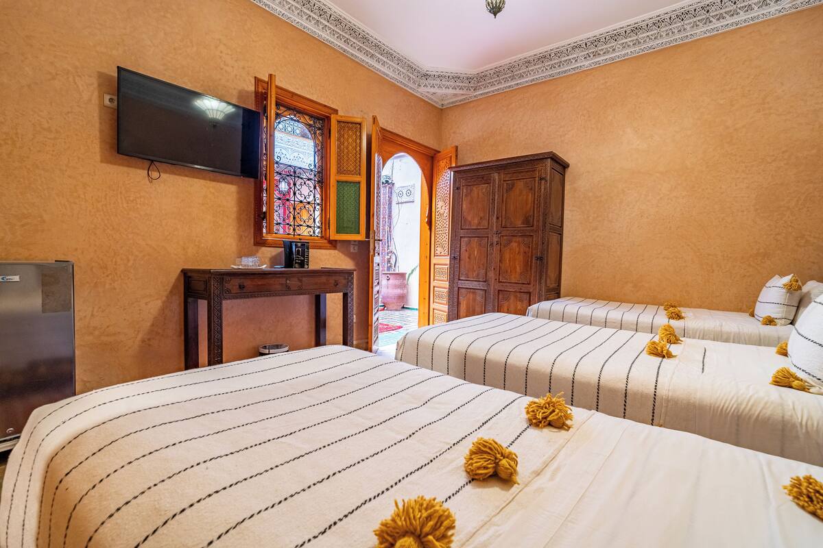 Une chambre d’hôtel avec deux lits, une télévision, une armoire en bois et une fenêtre décorative.