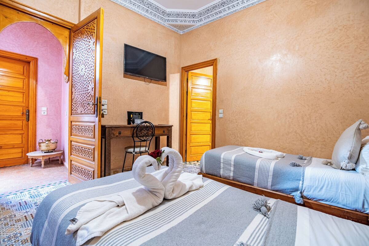 Une chambre d’hôtel avec deux lits, un bureau avec une chaise, une télévision et un panneau décoratif au mur.
