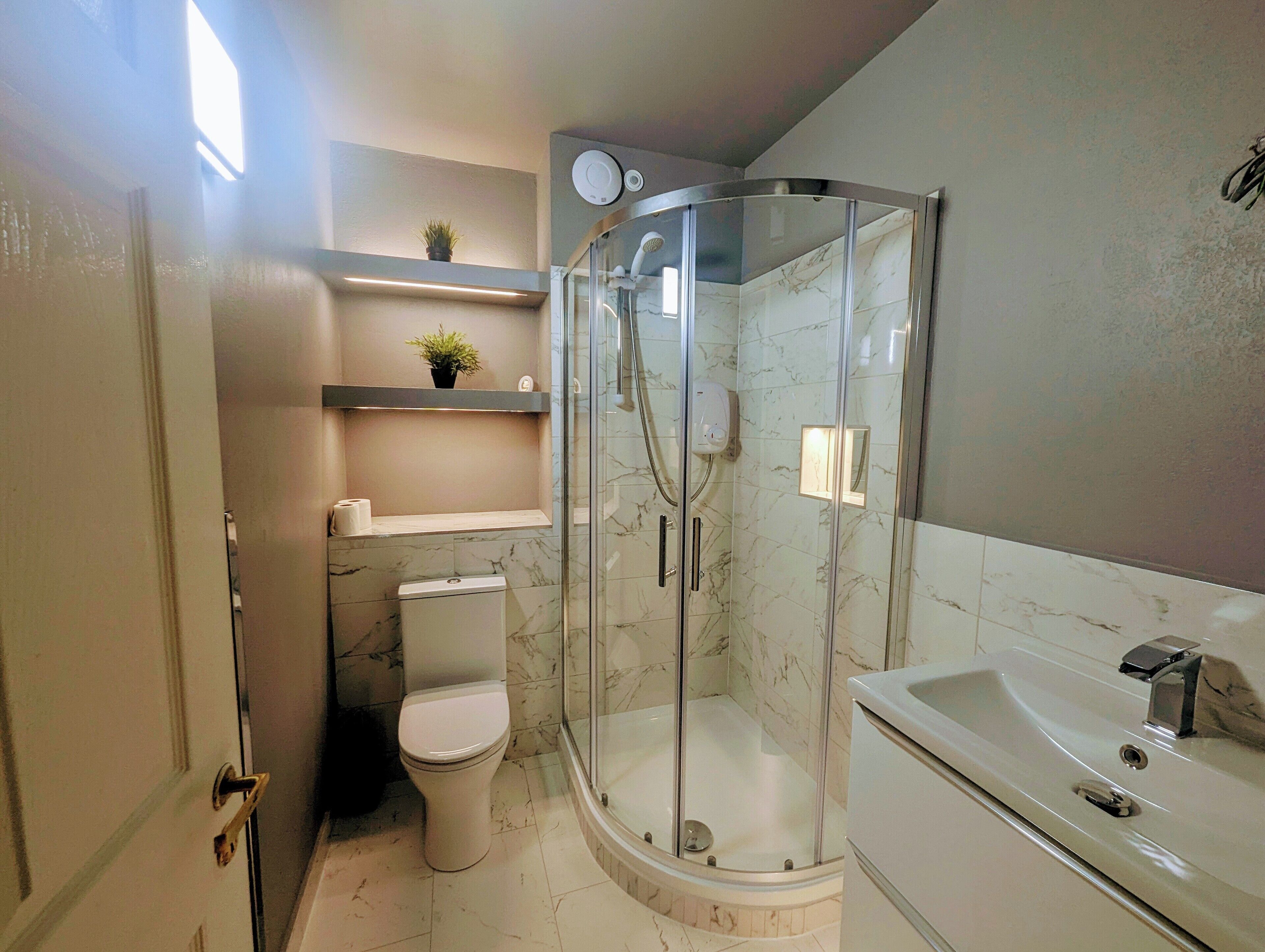 Un baño moderno con ducha envuelta en vidrio, inodoro, lavamanos y piso de mármol.