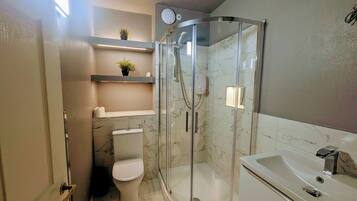 Un baño moderno con ducha envuelta en vidrio, inodoro, lavamanos y piso de mármol.