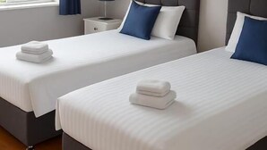 A hotel room with two beds, a nightstand, a lamp, and a view of the outdoors.