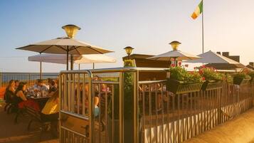 An outdoor dining area with tables and chairs, umbrellas, and a railing.