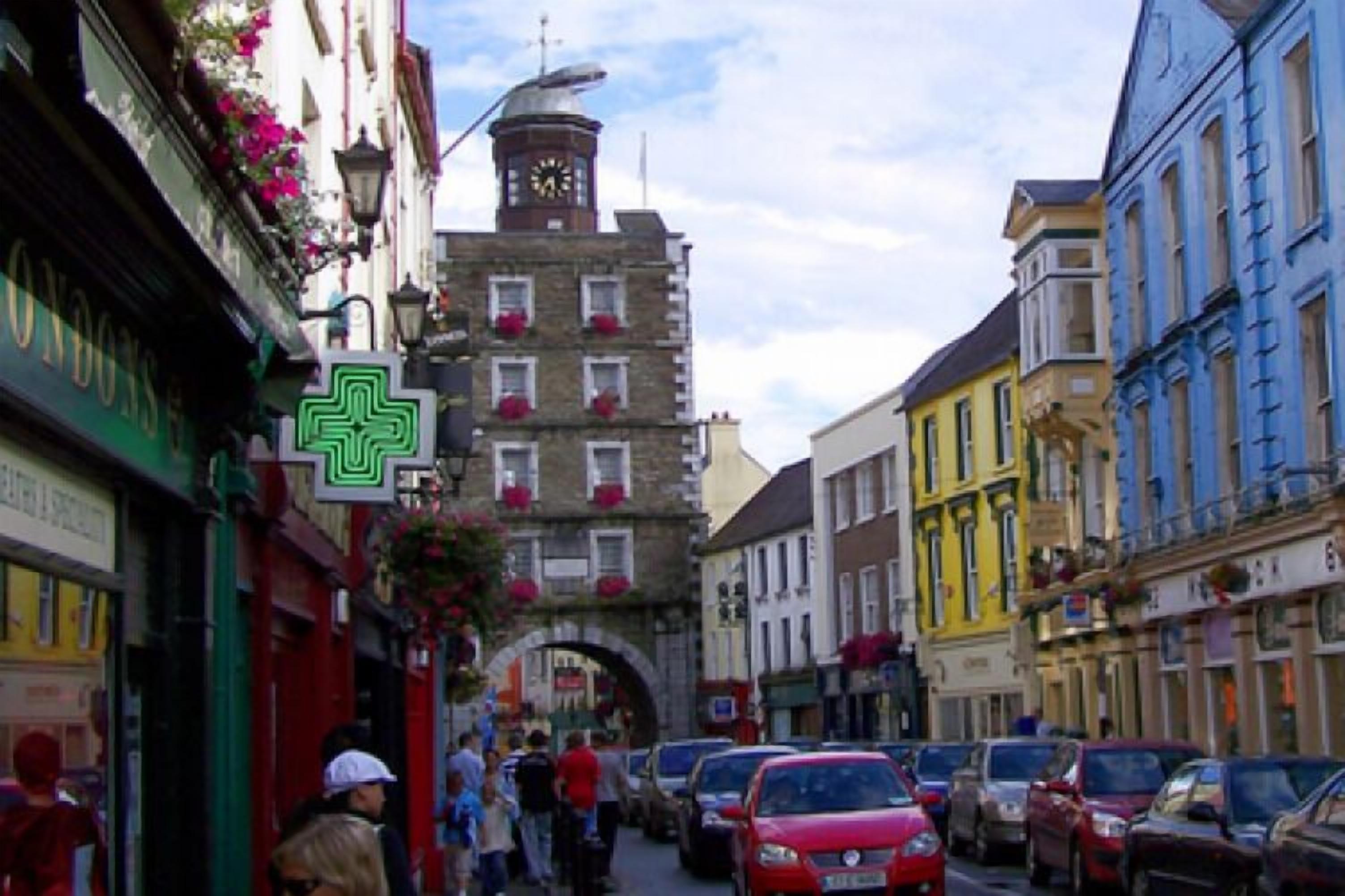 A narrow street lined with colorful buildings, a clock tower, and parked cars.