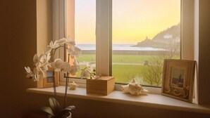 A window with a view of a coastal landscape, including a lighthouse and a grassy area.