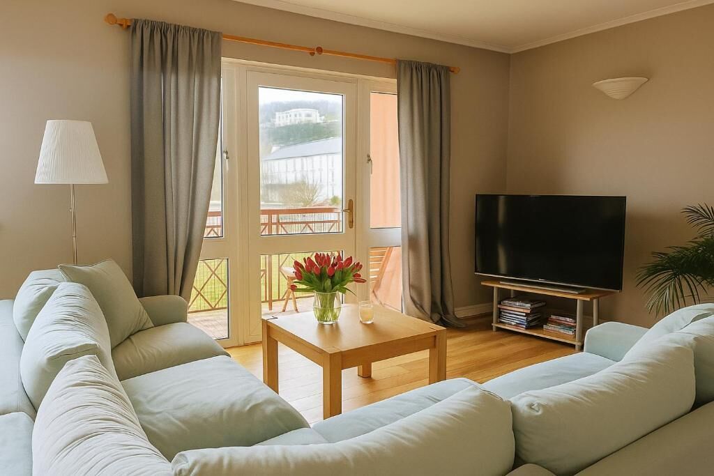 A living room with a sofa, a coffee table, a TV, and a balcony with curtains.