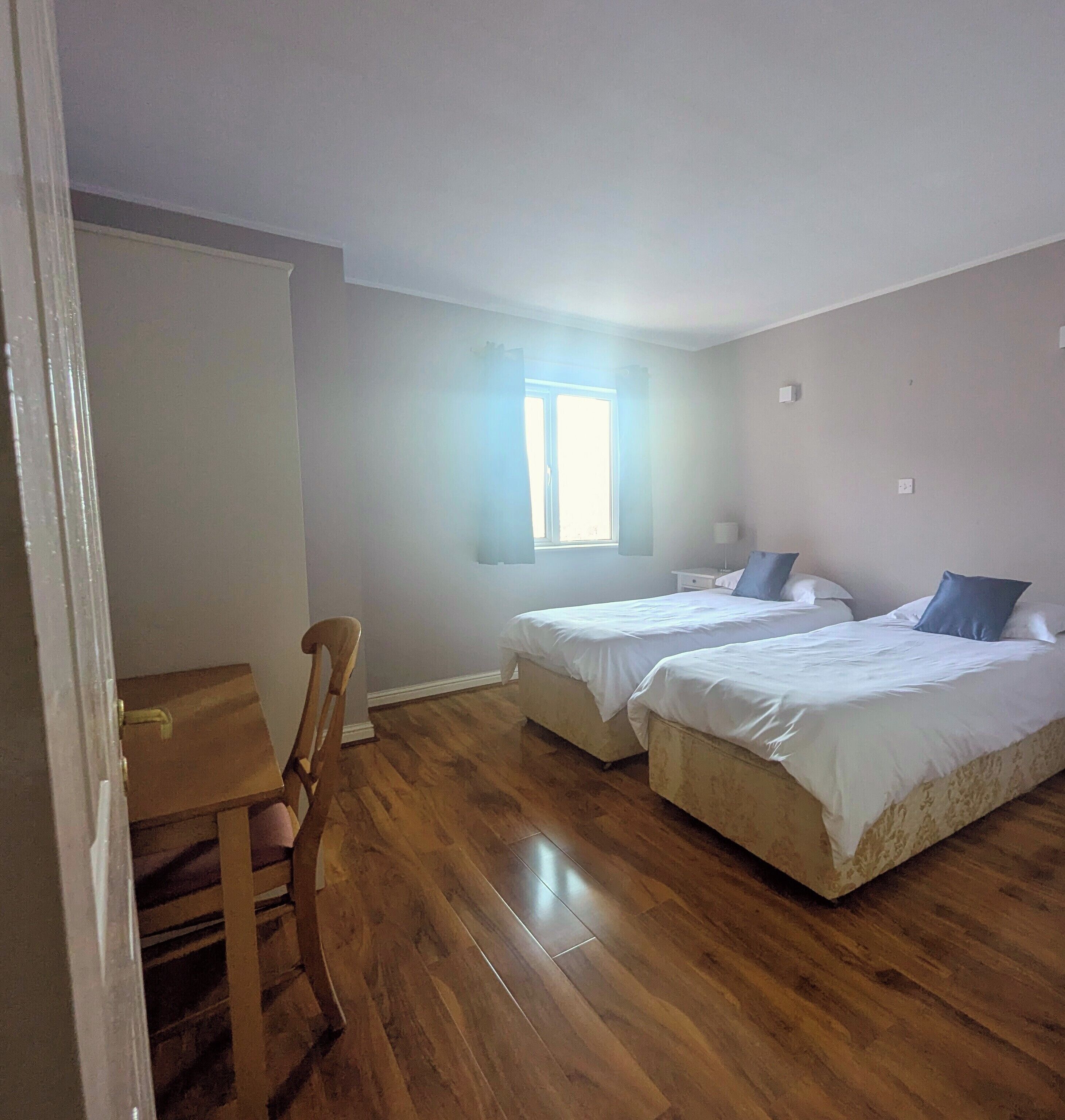 Una habitación con dos camas, una silla de madera, una mesita y una ventana.