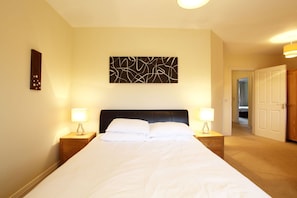 Un dormitorio de hotel con una cama grande, dos mesitas de noche con lámparas, una obra de arte abstracta en la pared y un armario de madera.