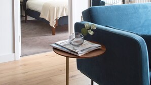 A modern living room with a blue sofa, a small round table with a glass, and a bed with a white headboard in the background. - London Islandic One Excel - O2 - Parking (London)