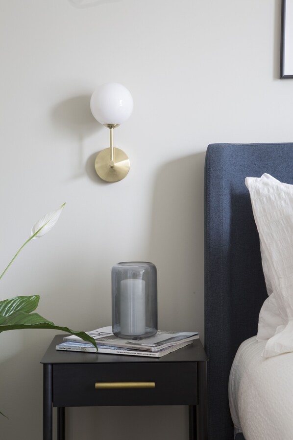 A neatly arranged bedroom with a bedside table, a lamp, a glass vase, and a bed.