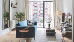 A modern living room with a blue sofa, a small round table, and a balcony with chairs. - London Islandic One Excel - O2 - Parking (London)