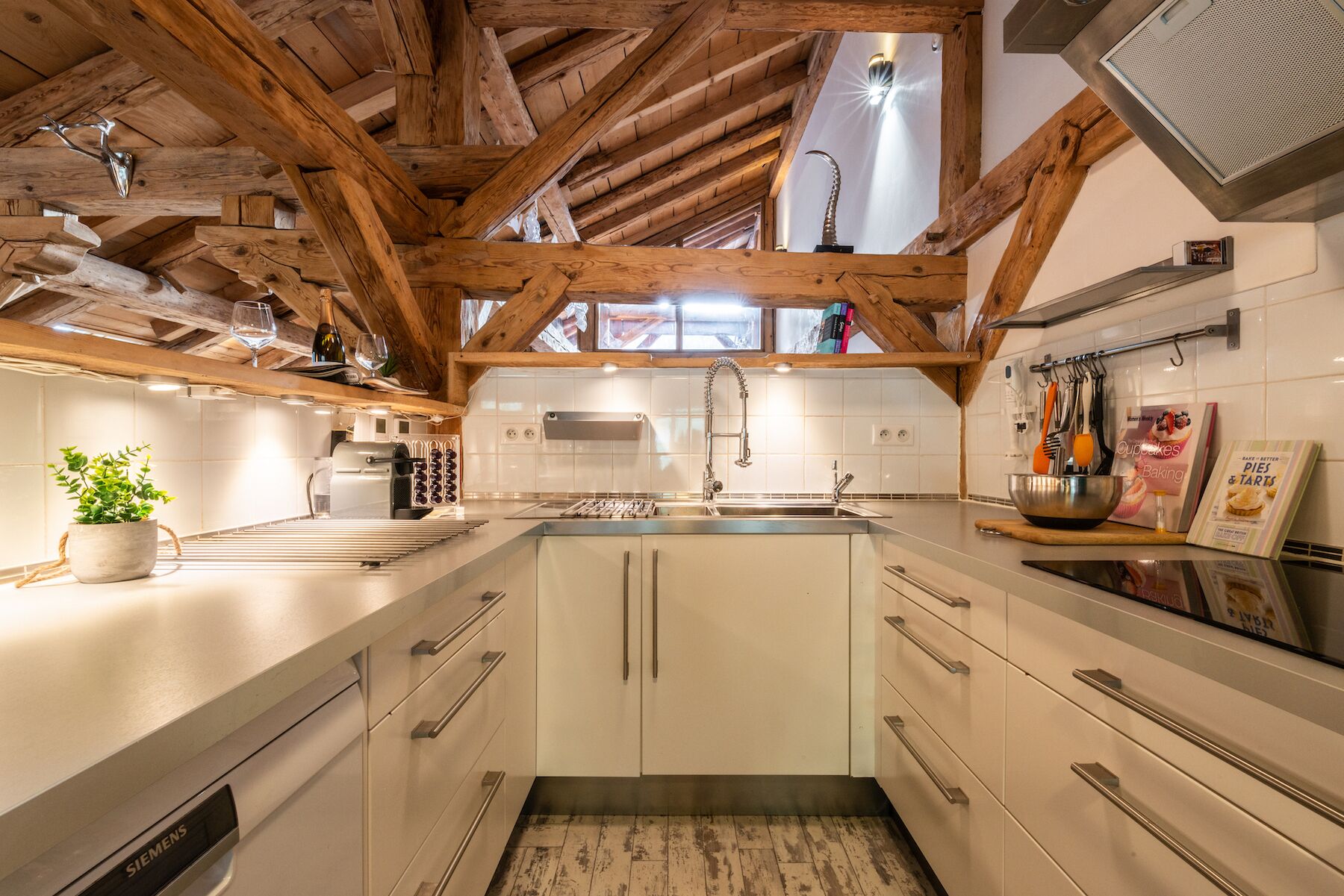A kitchen with wooden beams, white cabinets, a stainless steel sink, and a Siemens dishwasher.
