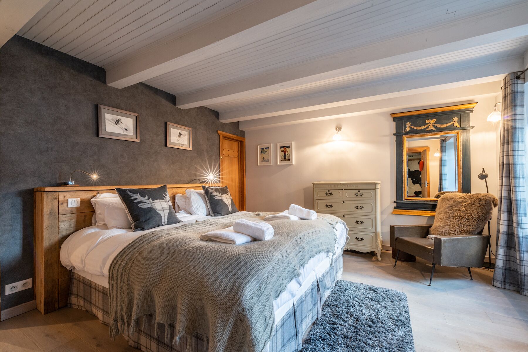 A bedroom with a large bed, a dresser, a chair, a mirror, and framed pictures on the wall.