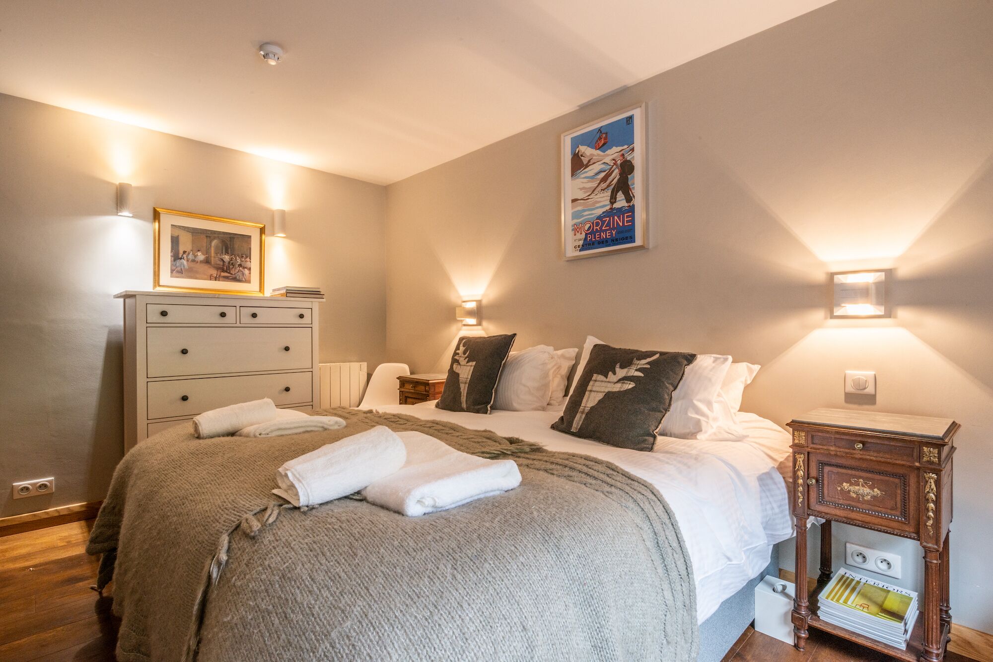 A hotel room with a bed, bedside tables, a dresser, and a poster on the wall.