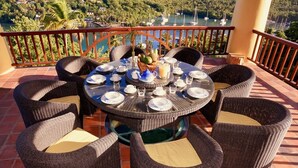 Une table de salle à manger ronde, entourée de huit chaises, mise pour un repas avec des assiettes, des tasses et un centre de table composé de fruits.