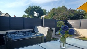 Una mesa con cubierta de vidrio, un jacuzzi, una silla y un florero con flores.