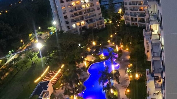 Un resort con una amplia piscina rodeada de palmeras y sillas de descanso, y varios edificios de hotel al fondo.