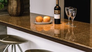 Una encimera de cocina con una botella de vino, dos copas y un plato con manzanas. Hay dos taburetes altos frente a la encimera.