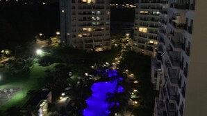 Vista nocturna de un hotel con varios edificios altos, una piscina iluminada y un área de estacionamiento bien iluminada.