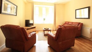 Een woonkamer met twee leren banken, een houten salontafel, een televisie op een dressoir en een radiator.