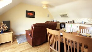 Een gezellige woonkamer met een bruine leren bank, een eettafel met stoelen, en een keuken met een fornuis en spoelbak.