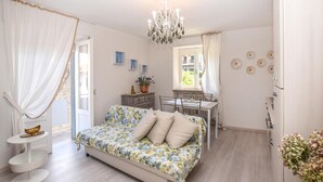 Un dormitorio con una cama, una mesita, una silla, una araña y una ventana con cortinas.