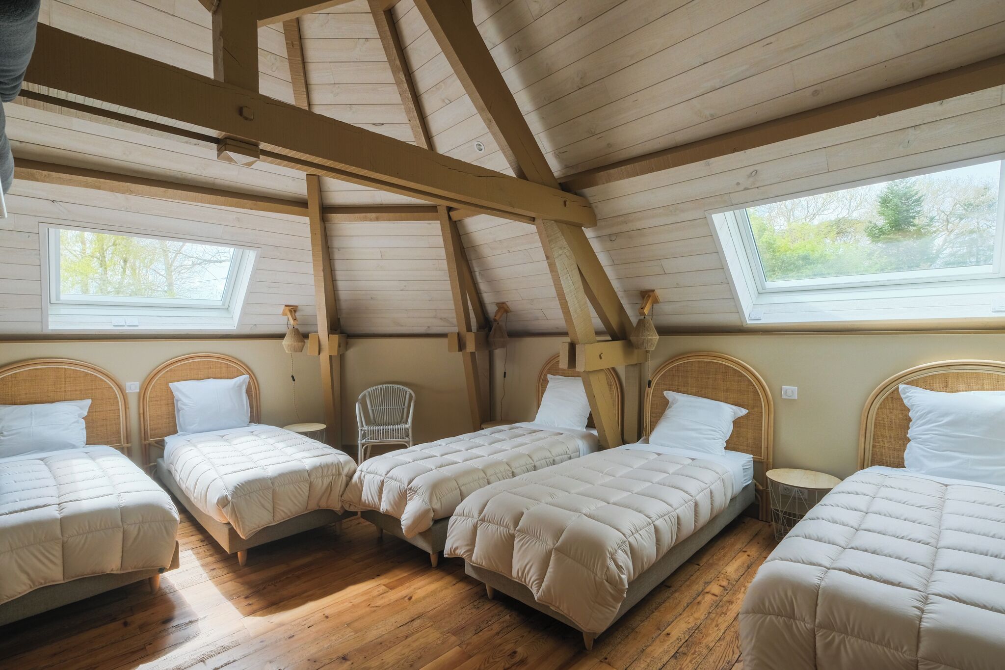 A room with four beds, wooden beams, skylights, and a small round table.