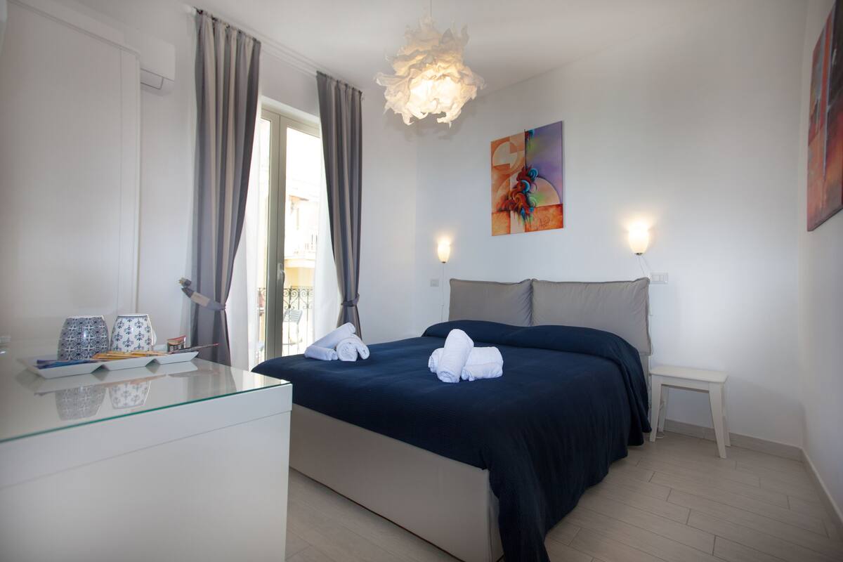 A modern bedroom with a bed, bedside tables, a glass dresser, and a view of the outside.