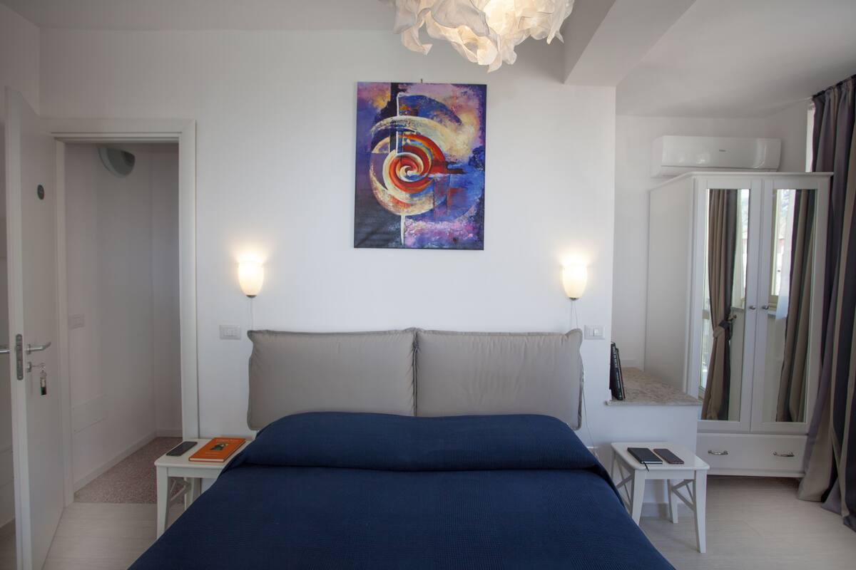 A bedroom with a large bed, bedside tables, a wall-mounted artwork, a wardrobe, and a ceiling light fixture.