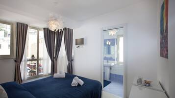 Ein Hotelzimmer mit einem großen Bett, einem Blick auf den Balkon, einem Badezimmer mit Waschbecken und Spiegel sowie einem Fernseher an der Wand.
