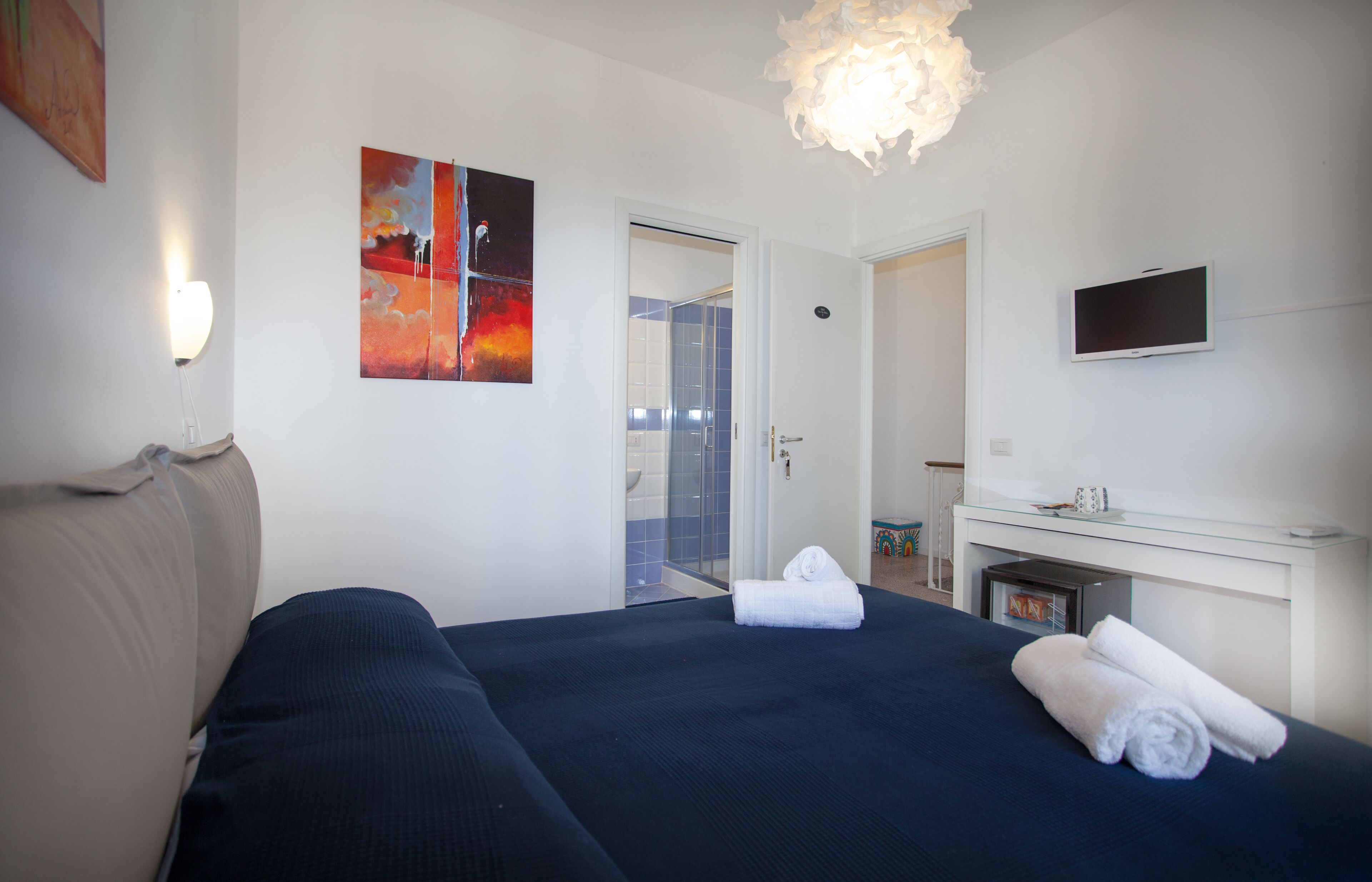 Ett hotellrum med en säng, en TV, en tavla och en duschhörna.