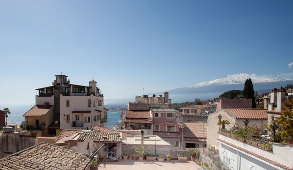 A coastal town with buildings overlooking the sea and a snow-capped mountain in the background. - Casa Don Micio (Taormina)