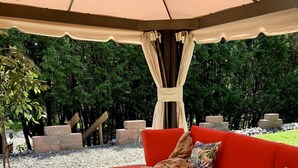 Een terras met een houten tafel en een rode bank onder een overkapping.