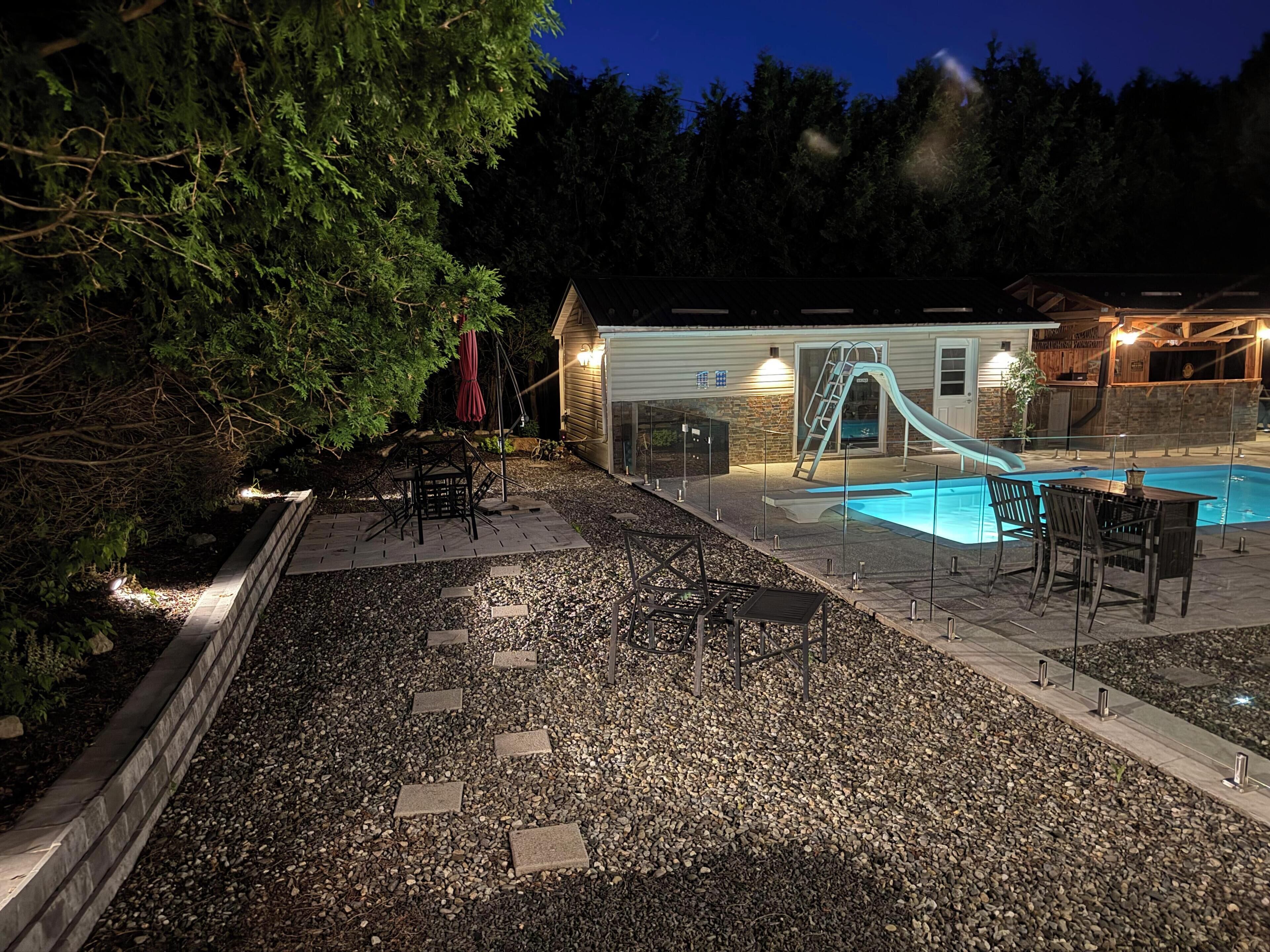 A swimming pool with a slide, surrounded by a patio area with chairs and tables.