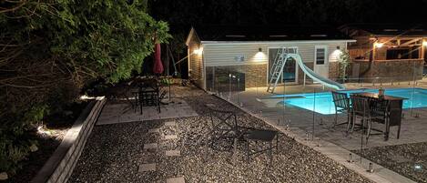 A swimming pool with a slide, surrounded by a patio area with chairs and tables.