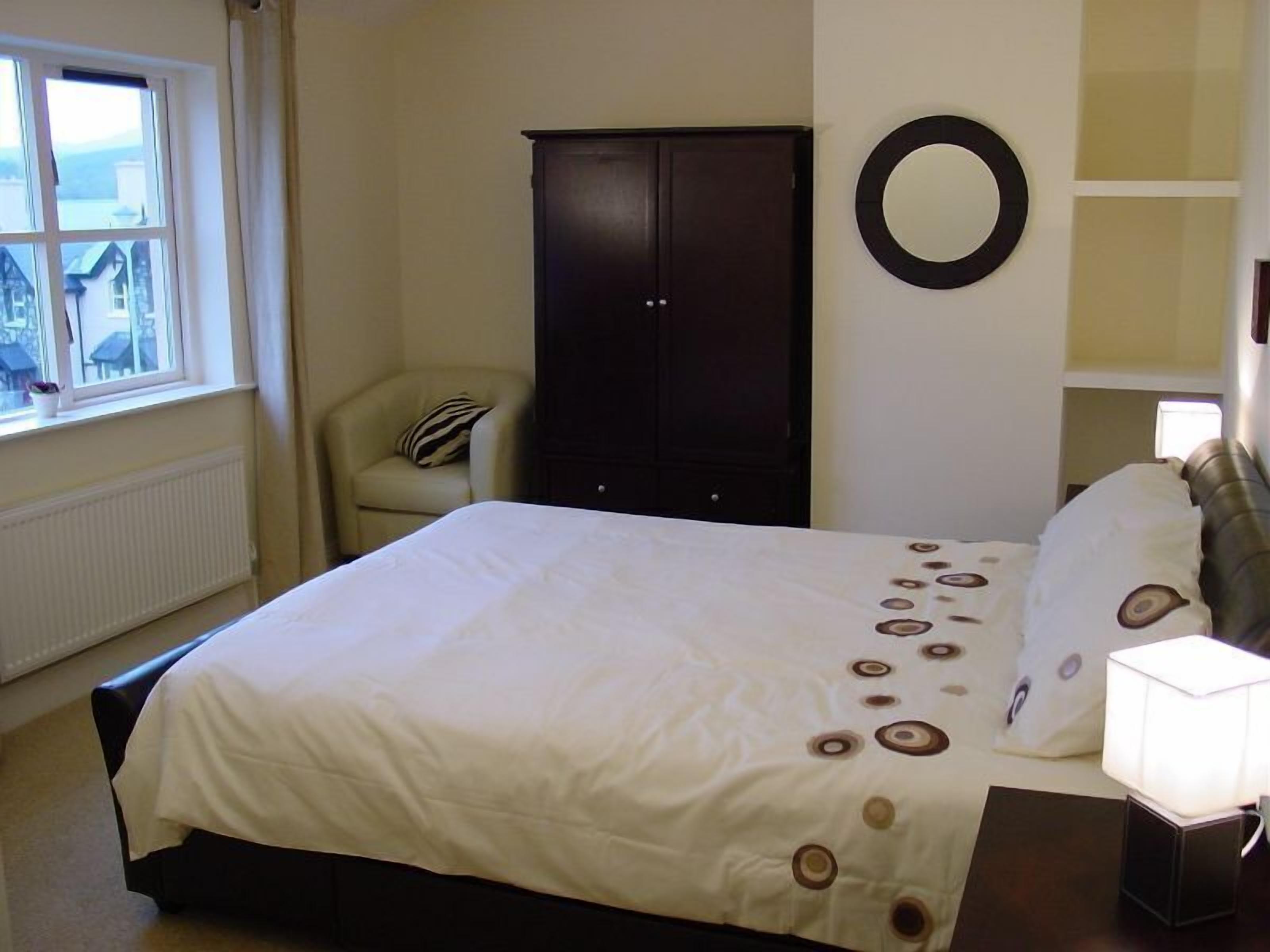 Un dormitorio con cama, una silla, armario, espejo redondo y lámpara de noche.